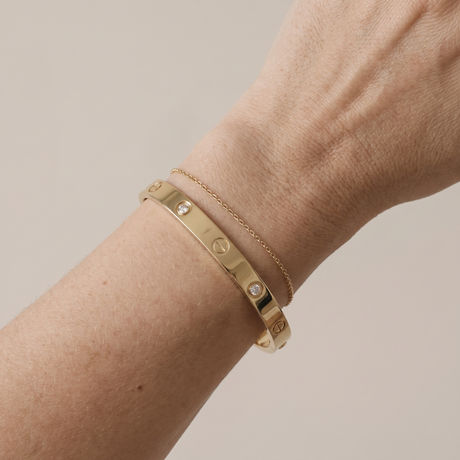 A gold-plated bangle and thin chain bracelet worn on a wrist